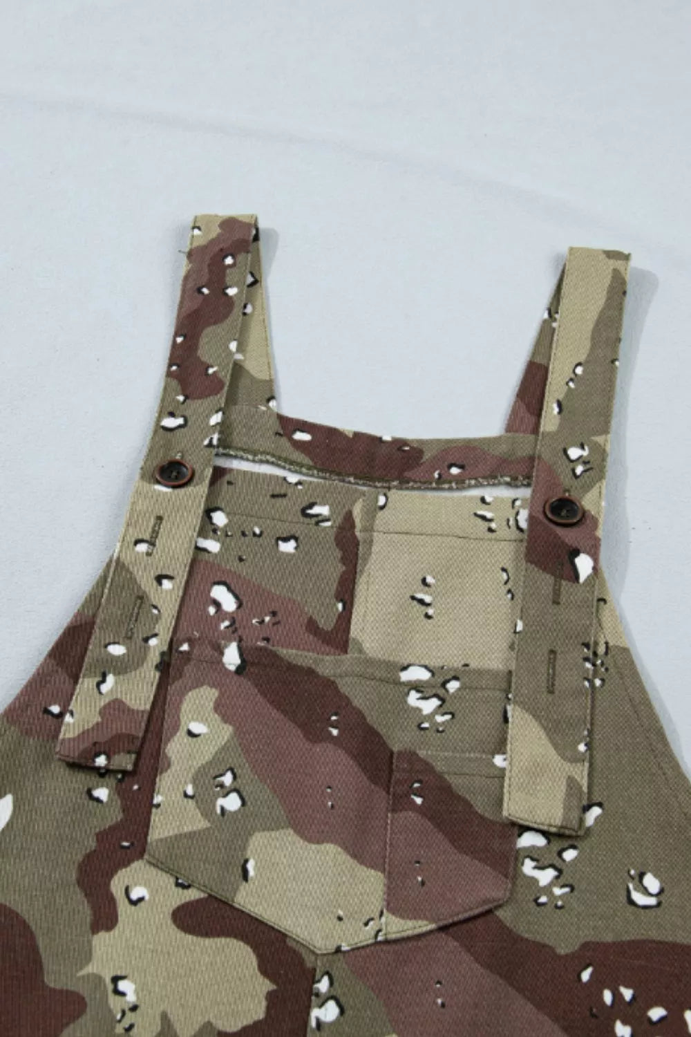 Close up view of the Blending In Overalls in green and brown camouflage with adjustable straps, bib pocket, side buttons, and cropped wide legs.