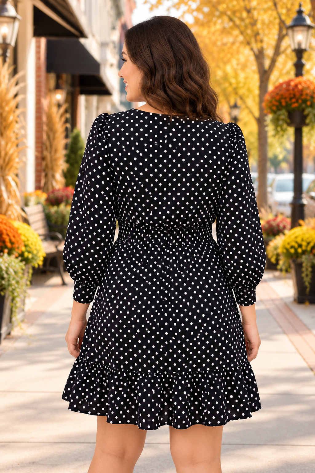 The Ever Changing Mini Dress in black with white polka dots, a wrap V-neck, tie waist, long sleeves, and ruffled hem back view.