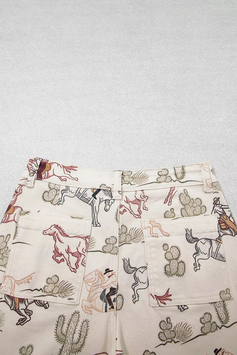Back view close up of the Rodeo Revival Jeans in cream with a cowboy, horse, and cactus print, high waist, and wide legs.