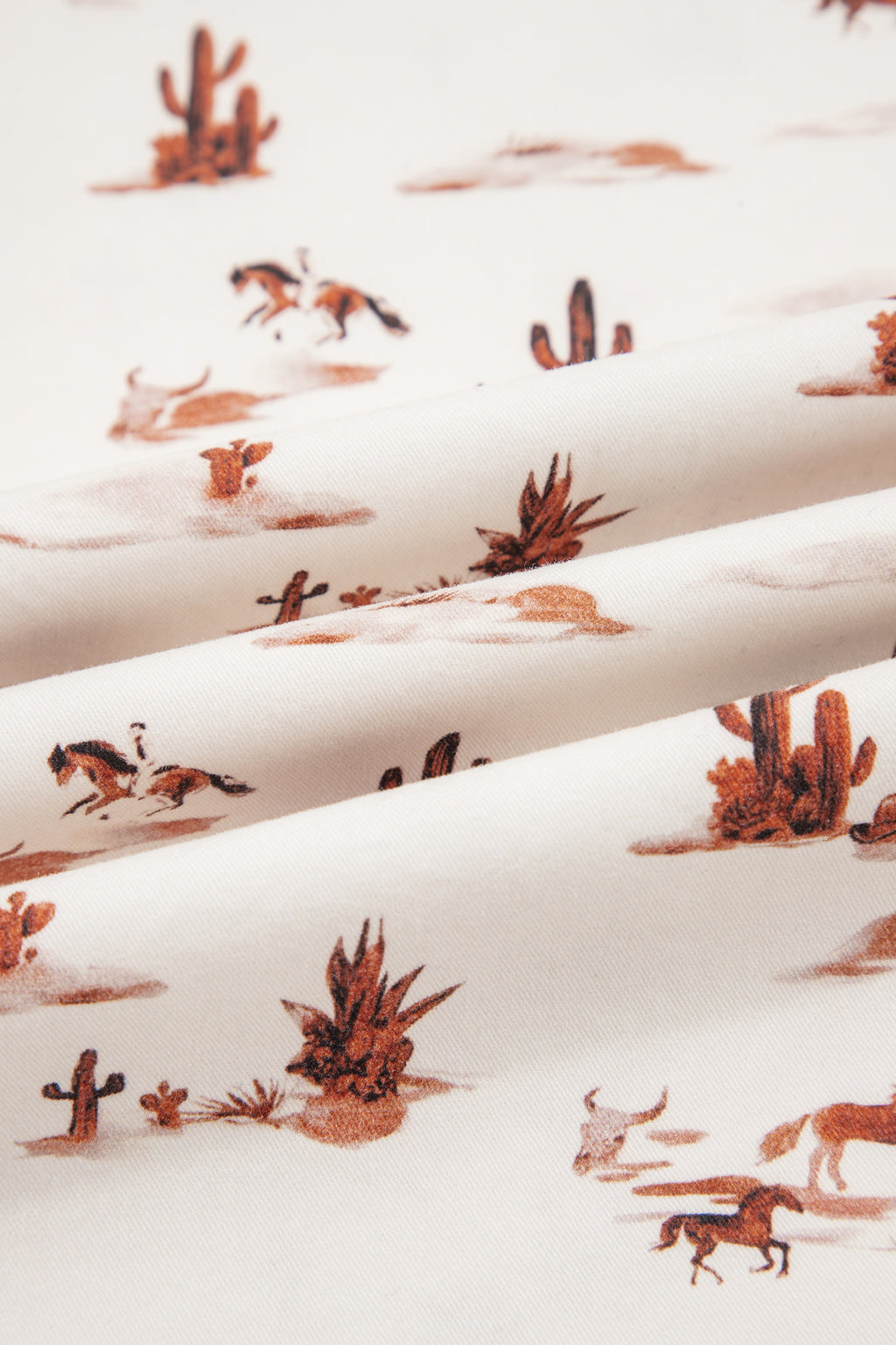 Close up pattern view of The Cowboy Way Overalls in cream with a Western desert print, adjustable straps, bib pocket, and wide legs.
