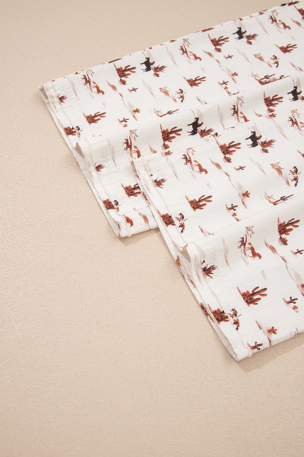 Hem view of The Cowboy Way Overalls in cream with a Western desert print, adjustable straps, bib pocket, and wide legs.
