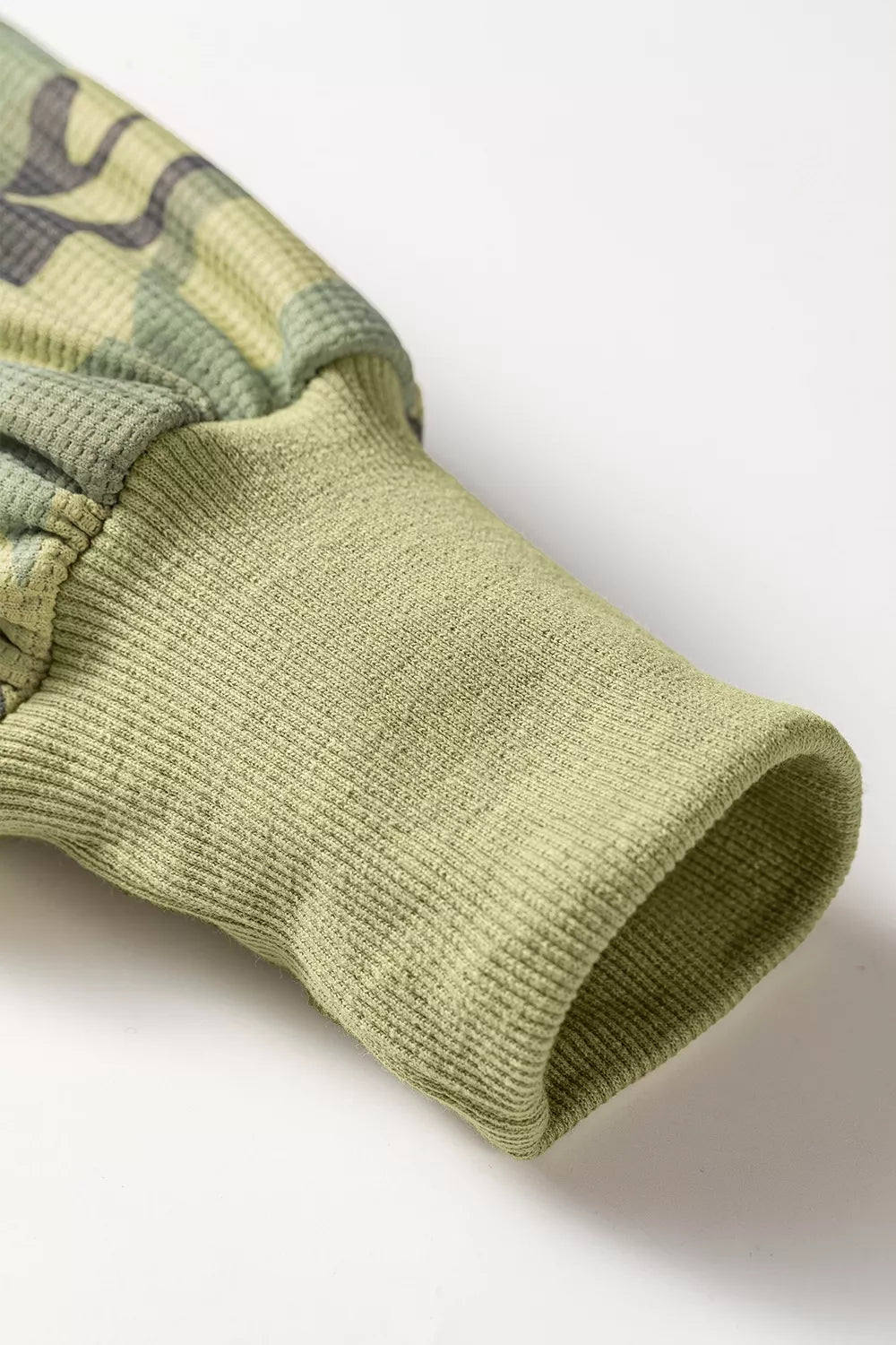 Cuff view of the Say It In Camo Top in green camouflage with textured fabric, exposed seams, long sleeves, and side slits.