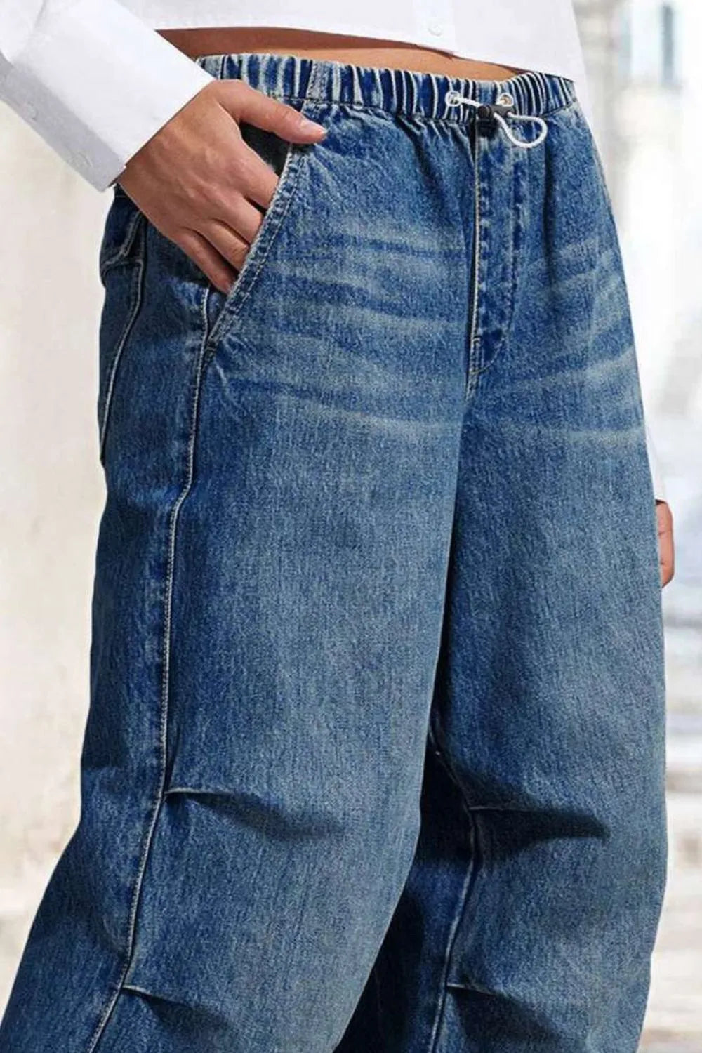 Jeans, high-waist, medium vintage wash, raw hem, front pockets, back flap pockets, wide leg, relaxed fit, elastic drawstring waist, shirred, slightly stretchy, side view close up