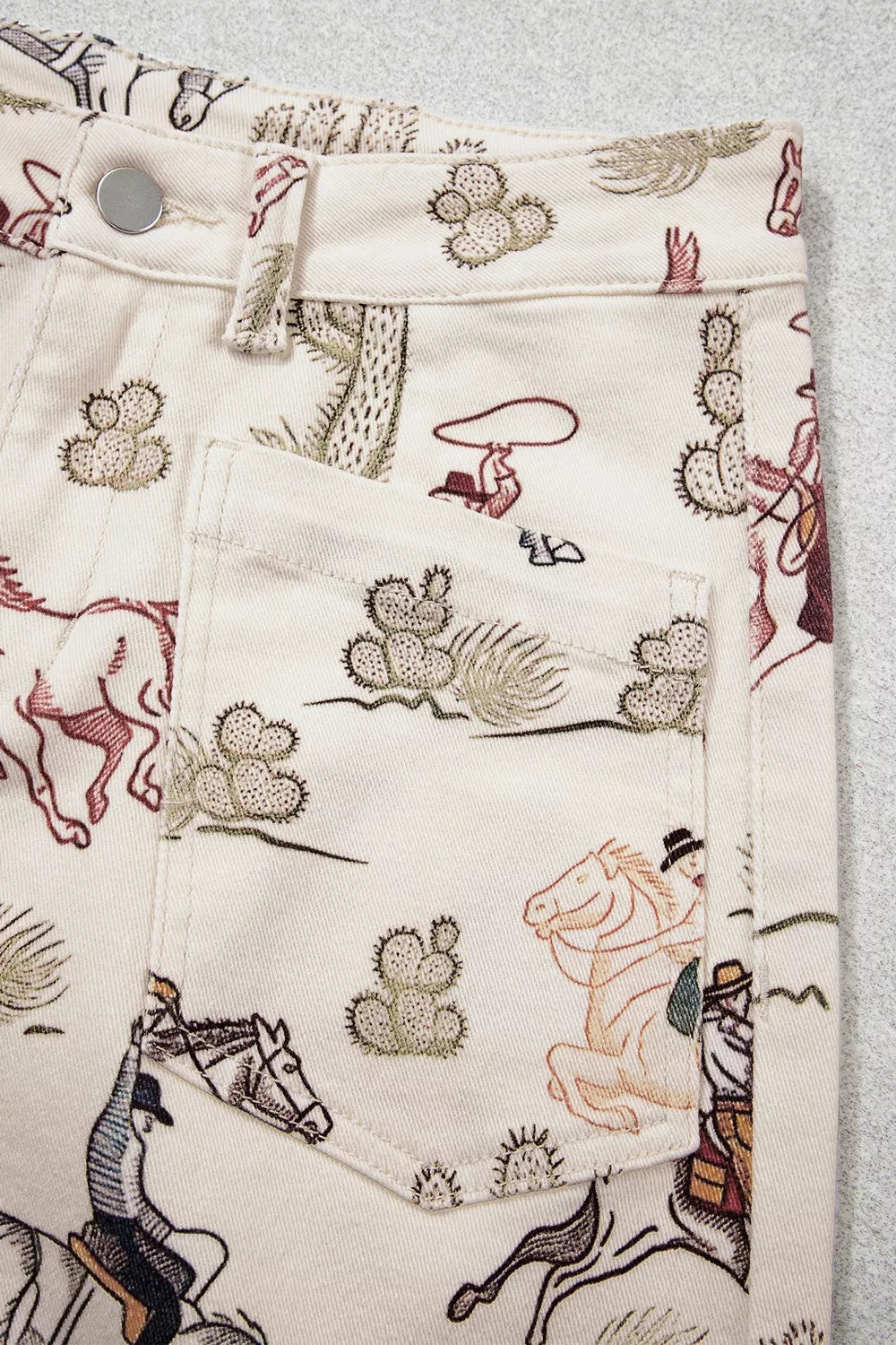 Front view close up of the Rodeo Revival Jeans in cream with a cowboy, horse, and cactus print, high waist, and wide legs.