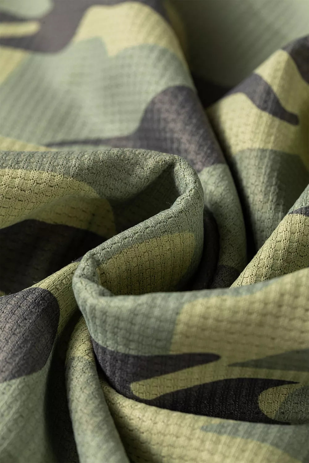 Close up view of the Say It In Camo Top in green camouflage with textured fabric, exposed seams, long sleeves, and side slits.