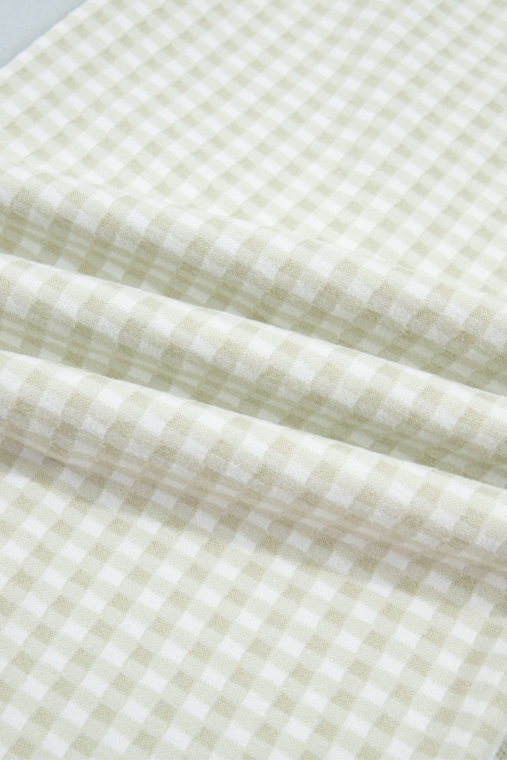 The Reece Pants in light green and cream gingham with wide cuffed legs, a drawstring waist, front pockets, and vertical seams close up view of fabric.