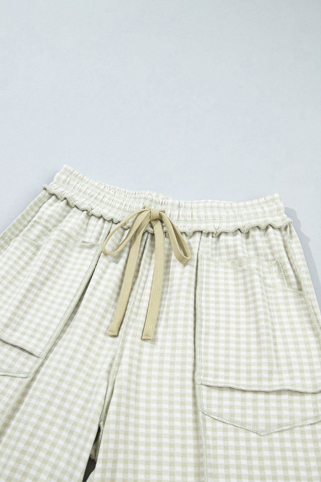 The Reece Pants in light green and cream gingham with wide cuffed legs, a drawstring waist, front pockets, and vertical seams close up front waist view.