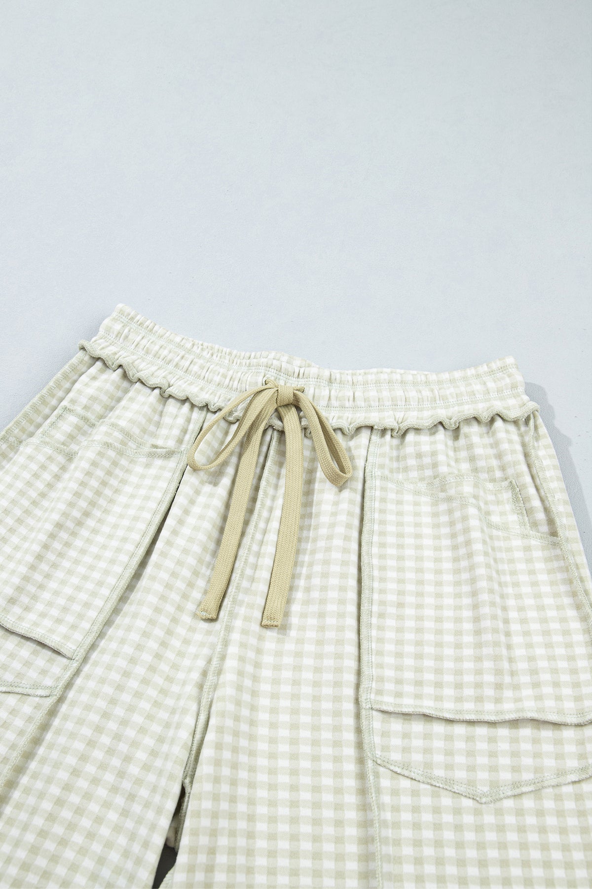 The Reece Pants in light green and cream gingham with wide cuffed legs, a drawstring waist, front pockets, and vertical seams close up front waist view.