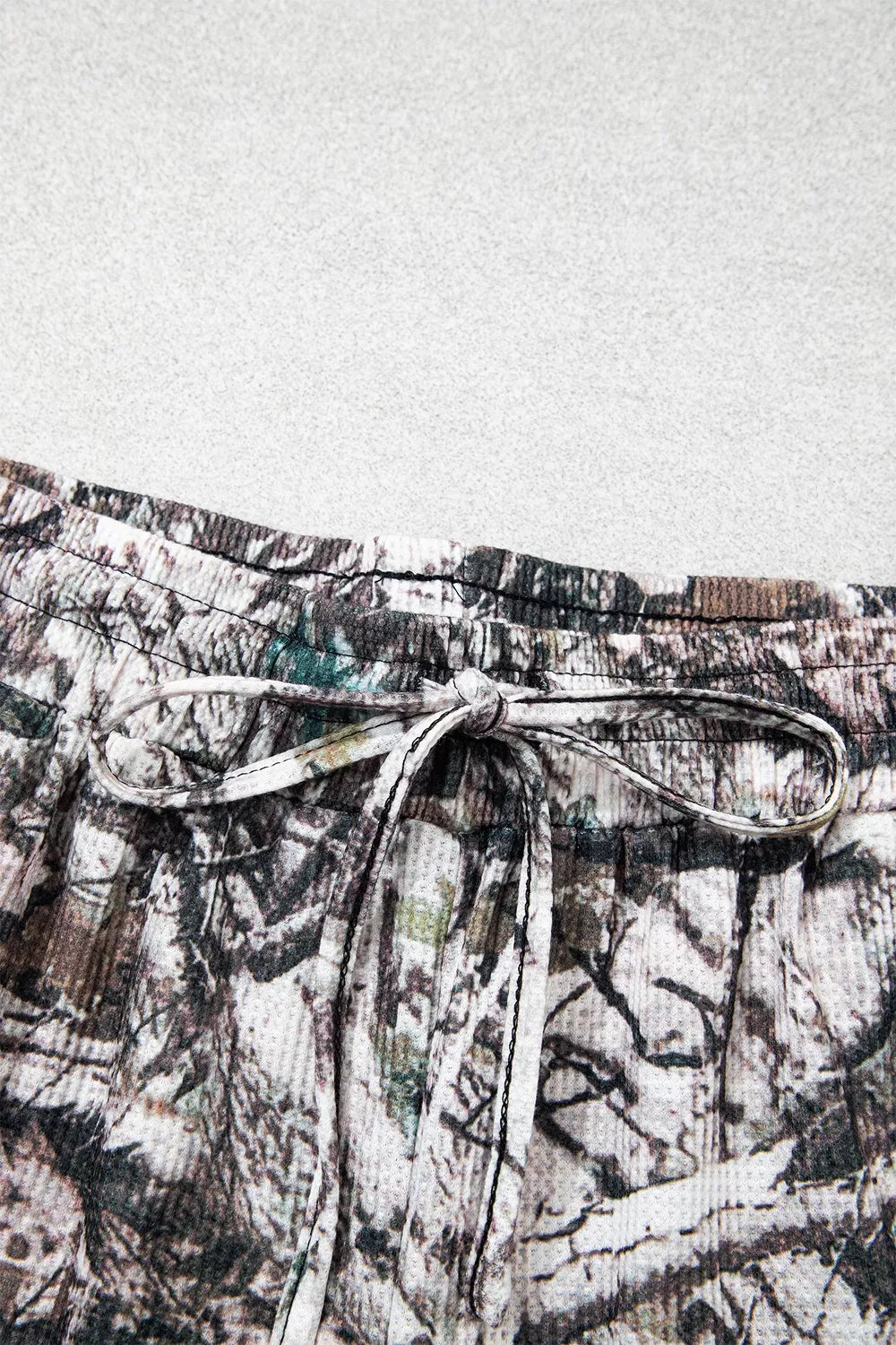 The Renegade Short Set in woodland camouflage with a long-sleeve button-front top and drawstring shorts with pockets close up view.