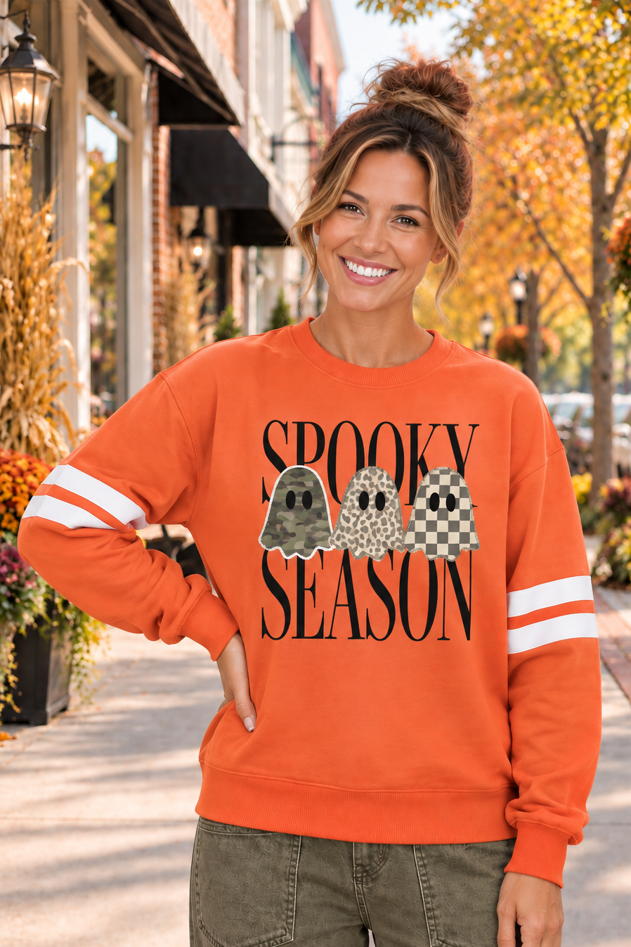 Spooky Season Graphic Sweatshirt in orange with varsity sleeve stripes and three patterned ghosts over black lettering, shown from the front.