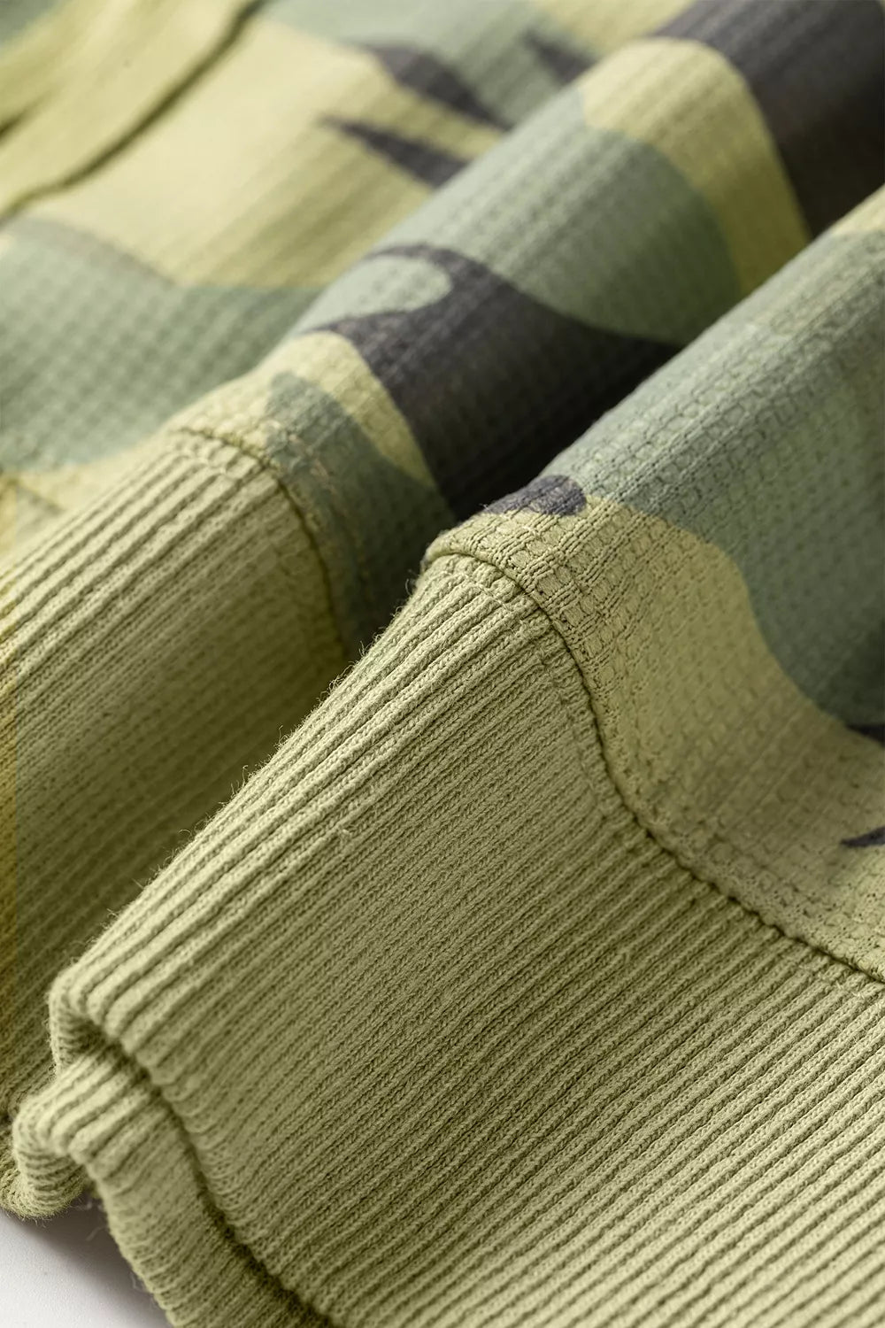 Hem view of the Say It In Camo Top in green camouflage with textured fabric, exposed seams, long sleeves, and side slits.