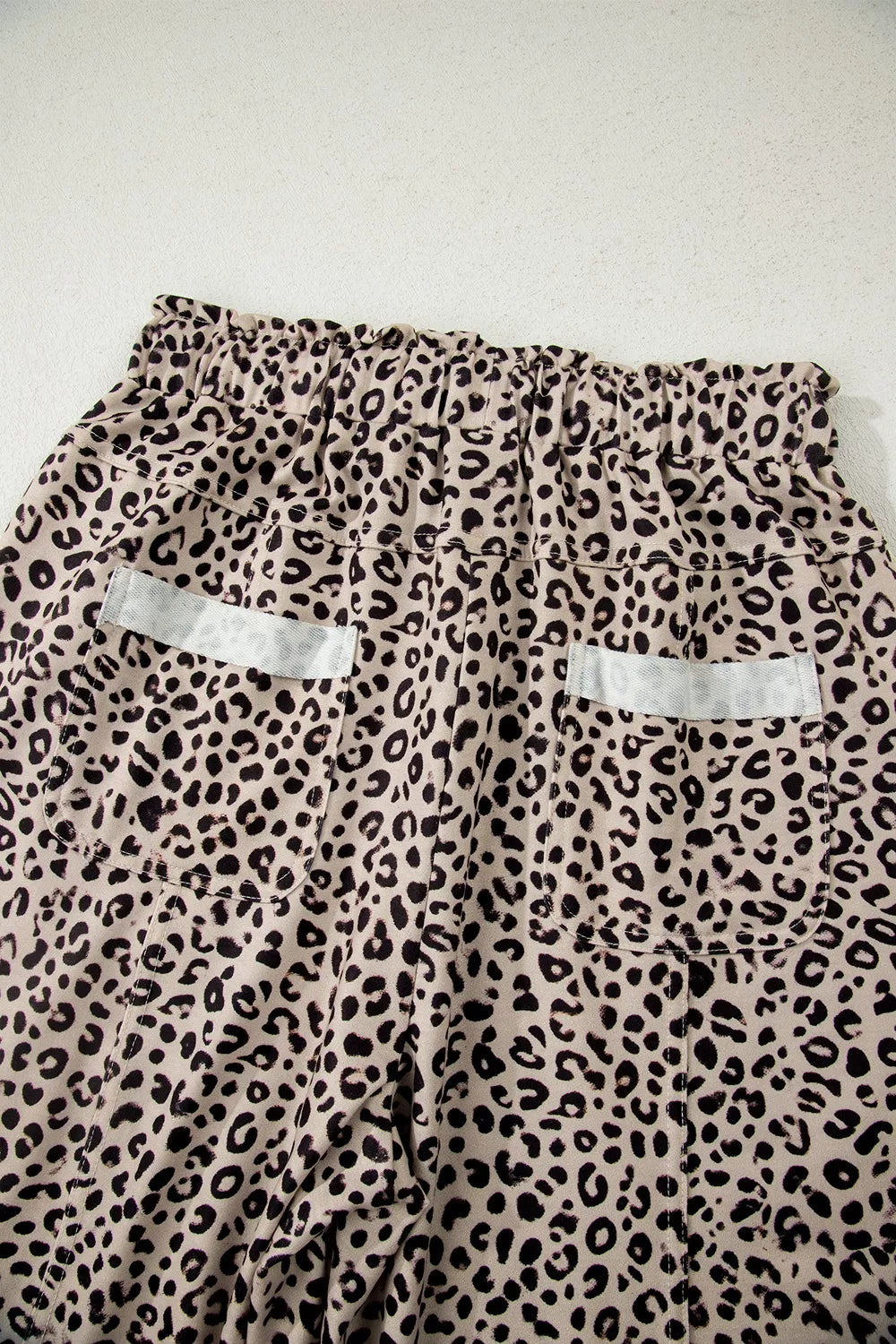 The Ziggy Pants in a beige and black leopard print with wide legs, a drawstring waist, and front patch pockets back view close up.