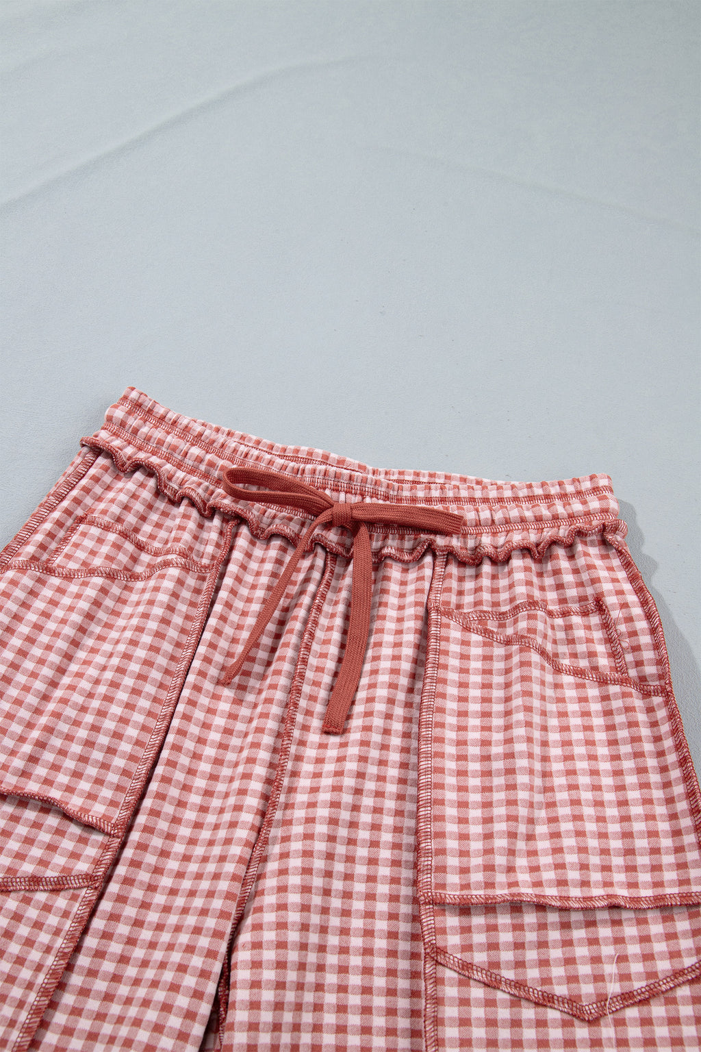 The Reece Pants in red and cream gingham with wide cuffed legs, a drawstring waist, front pockets, and vertical seams front close up view of waist.